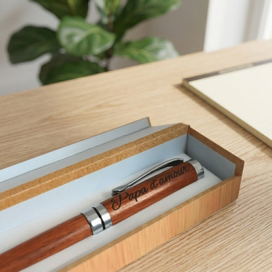 Stylo en bois rotatif gravé « Papa d'amour » dans son coffret ouvert à l'intérieur clair, sur une table en bois – Weastyle Gravure
