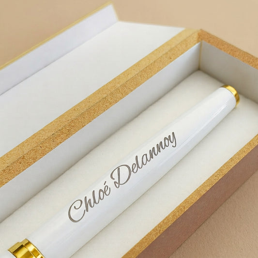 Gros plan sur la gravure « Chloé Delannoy » en lettres fines sur le stylo en métal blanc à finitions dorées, dans son coffret ouvert – Weastyle Gravure