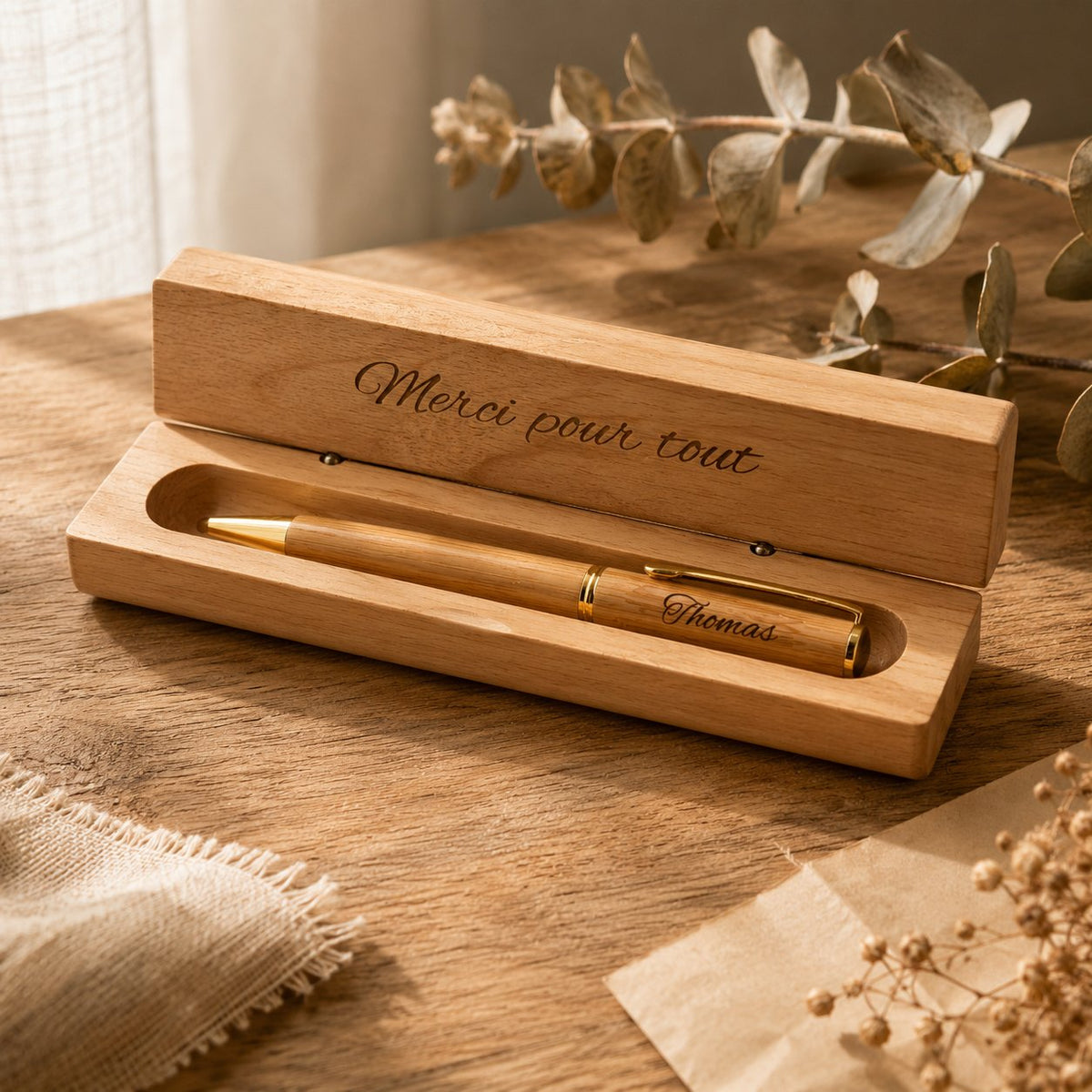 Coffret stylo en bois ouvert, couvercle gravé « Merci pour tout » et stylo à clip doré gravé « Thomas », sur une table en bois – Weastyle Gravure