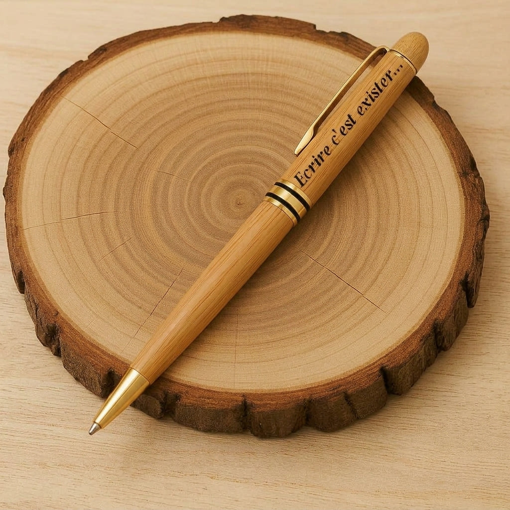 Stylo en bois aux finitions dorées gravé « Ecrire c'est exister… », posé sur un rondin de bois – Weastyle Gravure