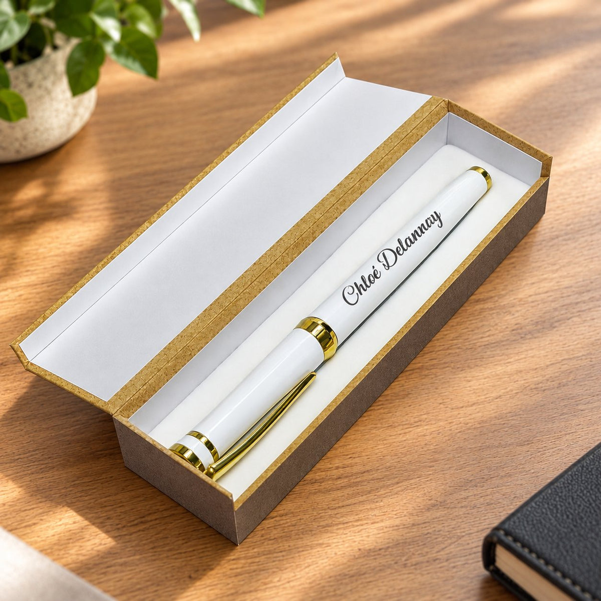 Stylo en métal blanc et doré gravé d'un prénom dans son coffret ouvert à couvercle relevé, vu de dessus sur une table en bois – Weastyle Gravure