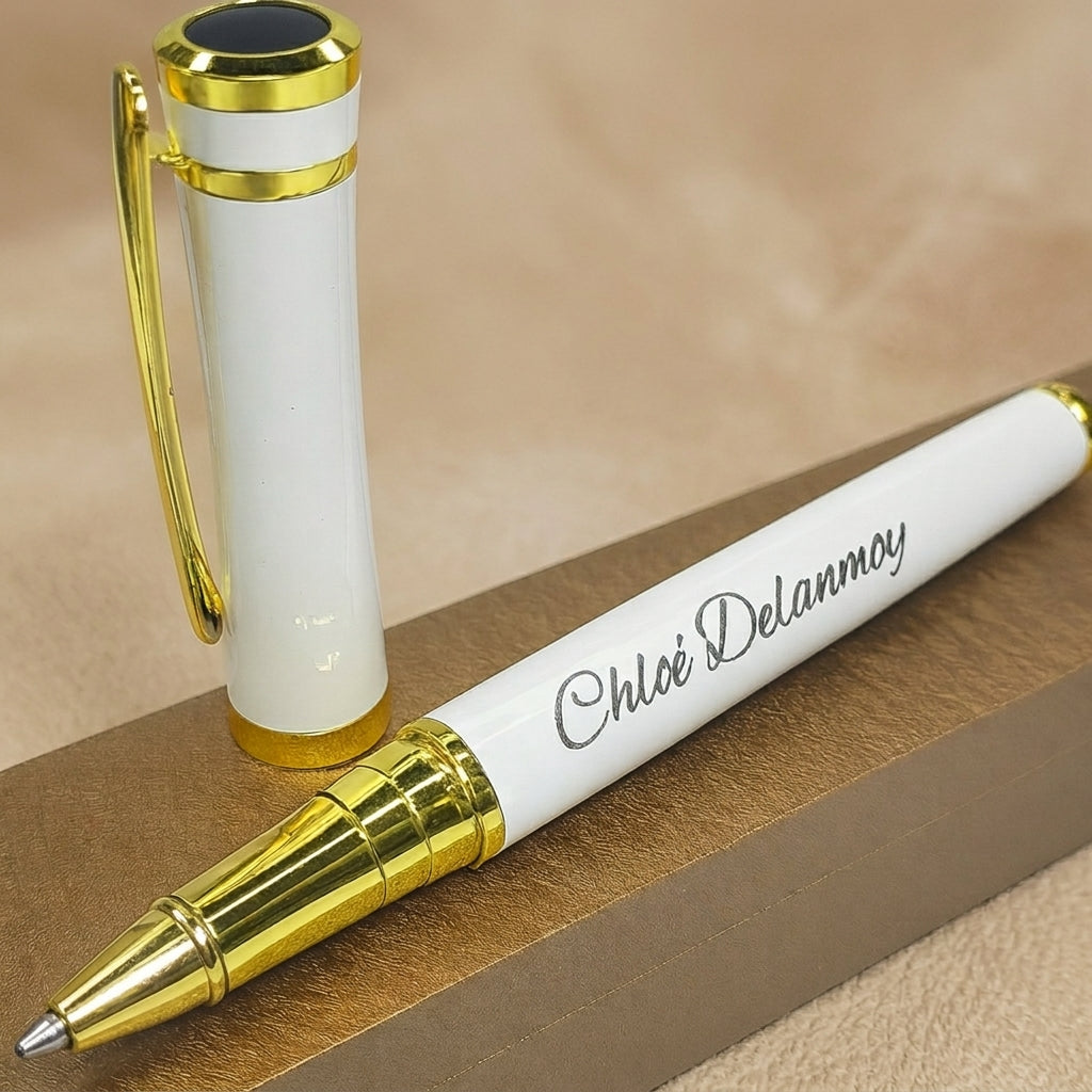 Stylo en métal blanc et doré, capuchon à clip doré retiré, gravé d'un prénom en lettres fines, posé sur un coffret brun métallisé – Weastyle Gravure