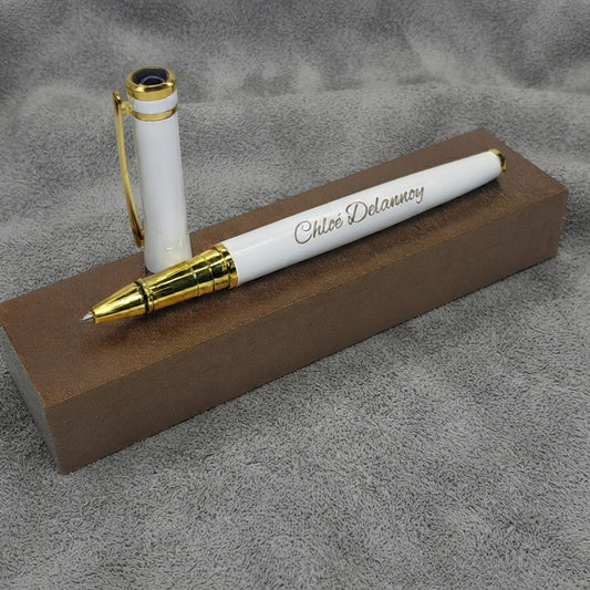 Stylo en métal blanc et doré gravé « Chloé Delannoy », capuchon à clip doré posé debout, sur un socle brun et un fond de feutre gris – Weastyle Gravure